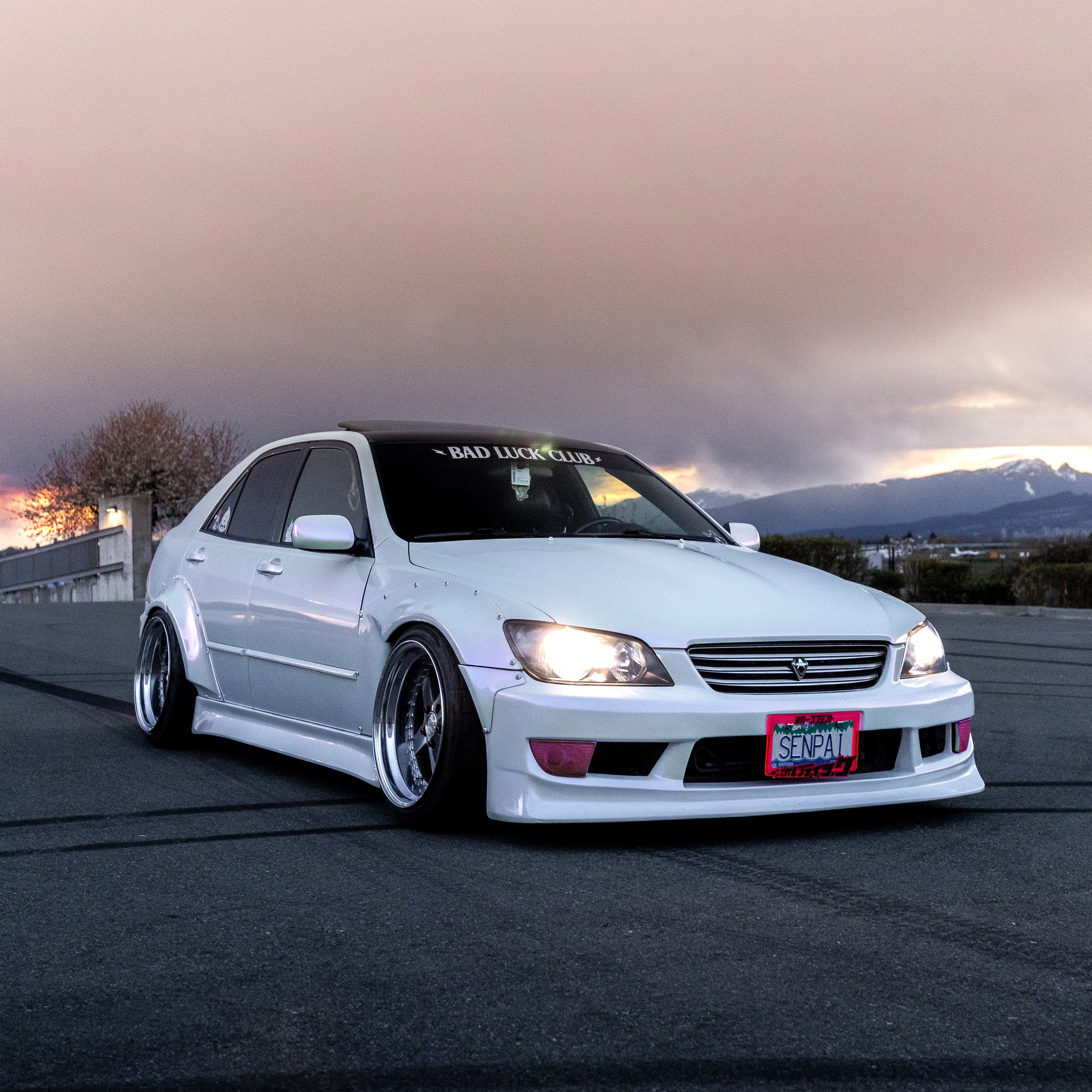 white widebody lexus is300 with vertex bodykit on wide 3 piece wheels. also known as a toyota altezza. car also has a senpai license plate