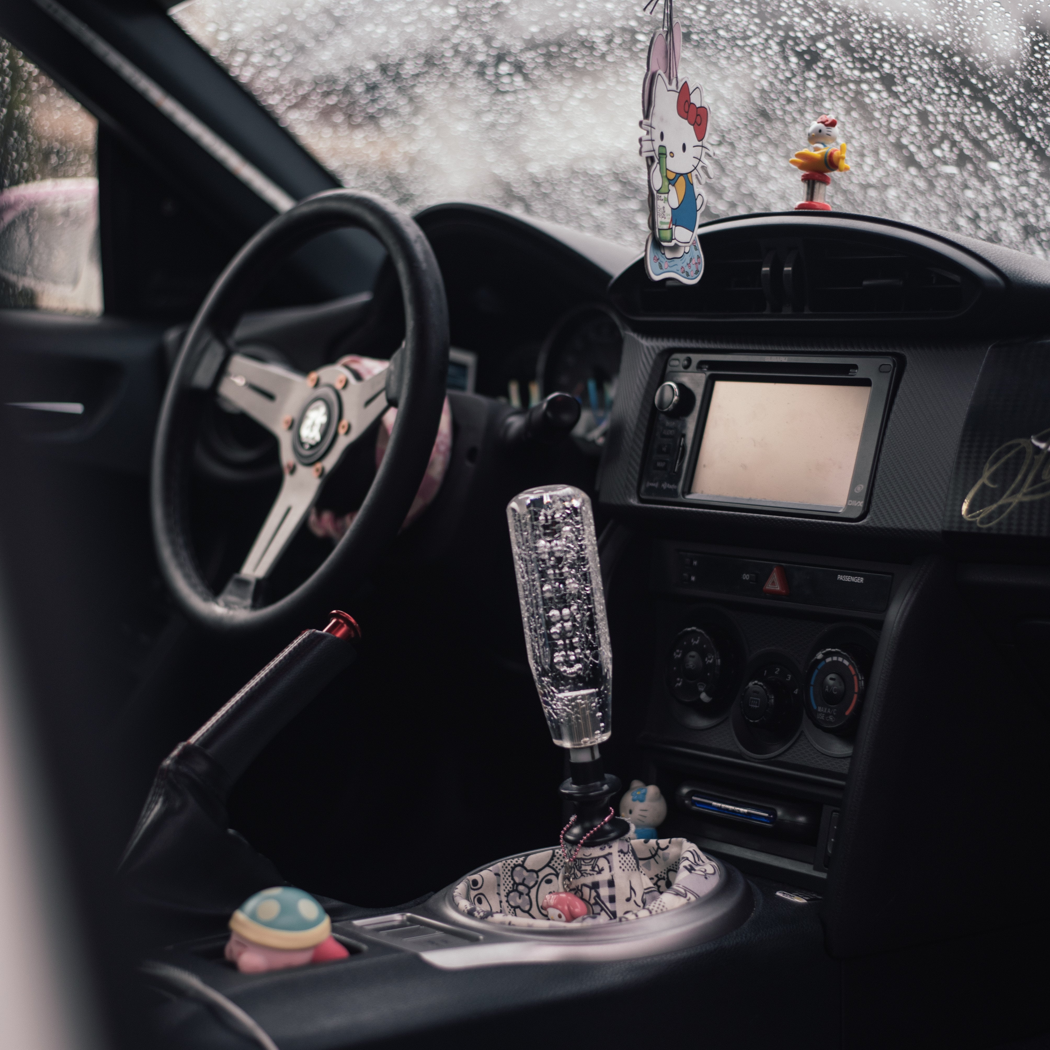 the interior of a subaru BRZ with a jdm bubble shift knob surrounded by lots of cute sanrio related car interior accessories